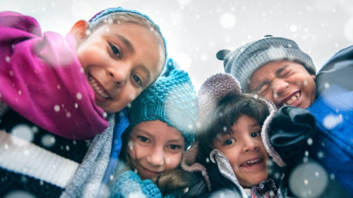 Group of kids wrapped up in warm clothes hugging outdoors in winter, low point of view.