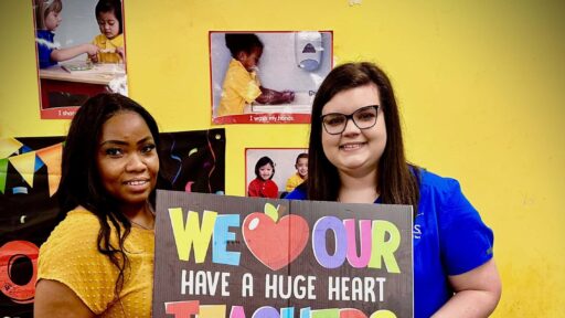 Two women stand next to each other holding a sign that says "We heart our Teachers. Have a Huge Heart"