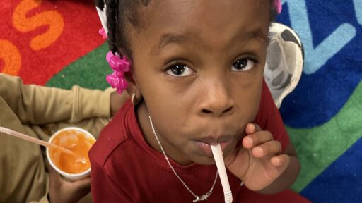 Child tasting carrot smoothie while looking at the camera