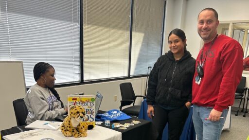 A parent is standing with our Multicultural Enrichment Specialist. A woman from Chicot Elementary is sitting at a table across from them.