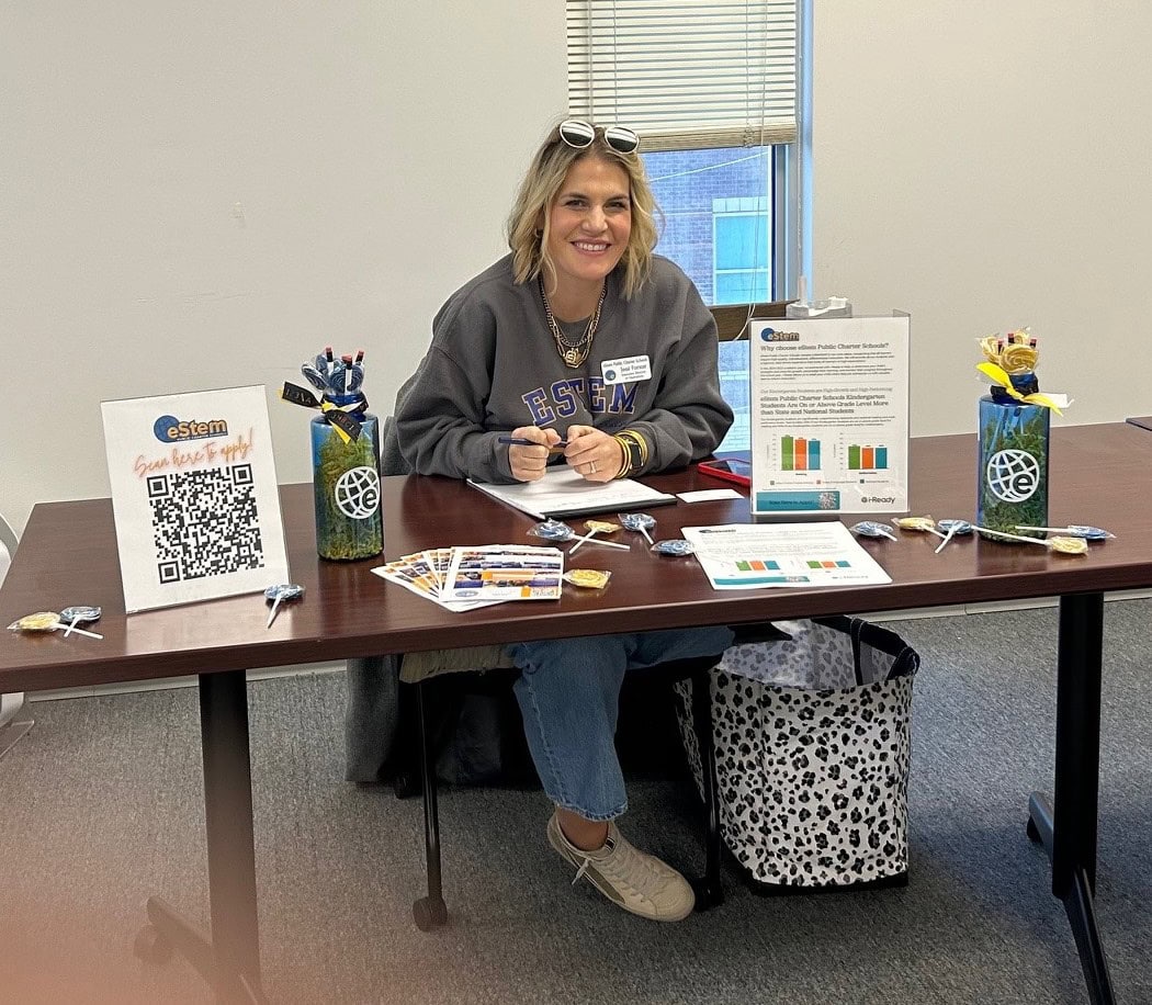 A woman from eStem school district is sitting at a table waiting to help parents with enrollment.