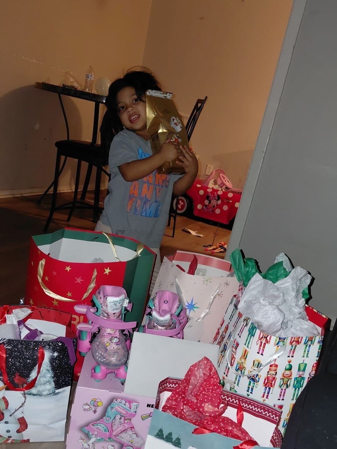 A boy stands holding a bag of chocolates and is behind bags and boxes with gifts.