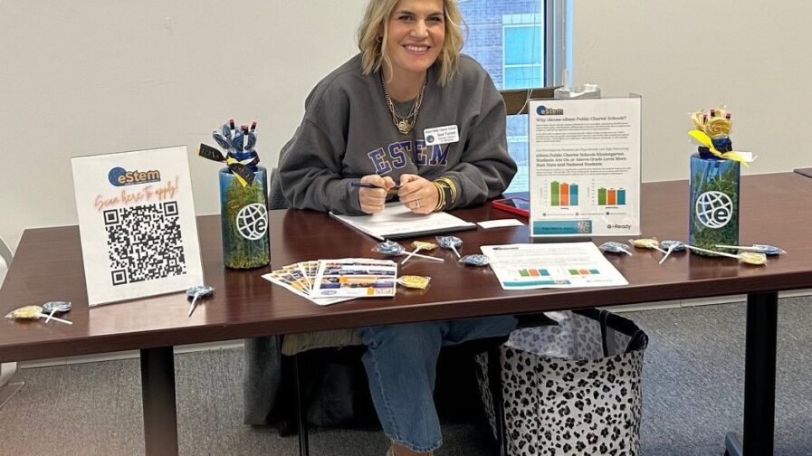 A woman from eStem school district is sitting at a table waiting to help parents with enrollment.