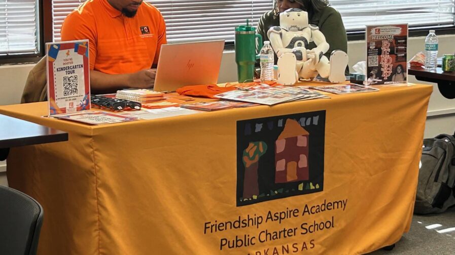 A man and woman from Friendship Aspire Academy are sitting at a table waiting to help families with enrollment.