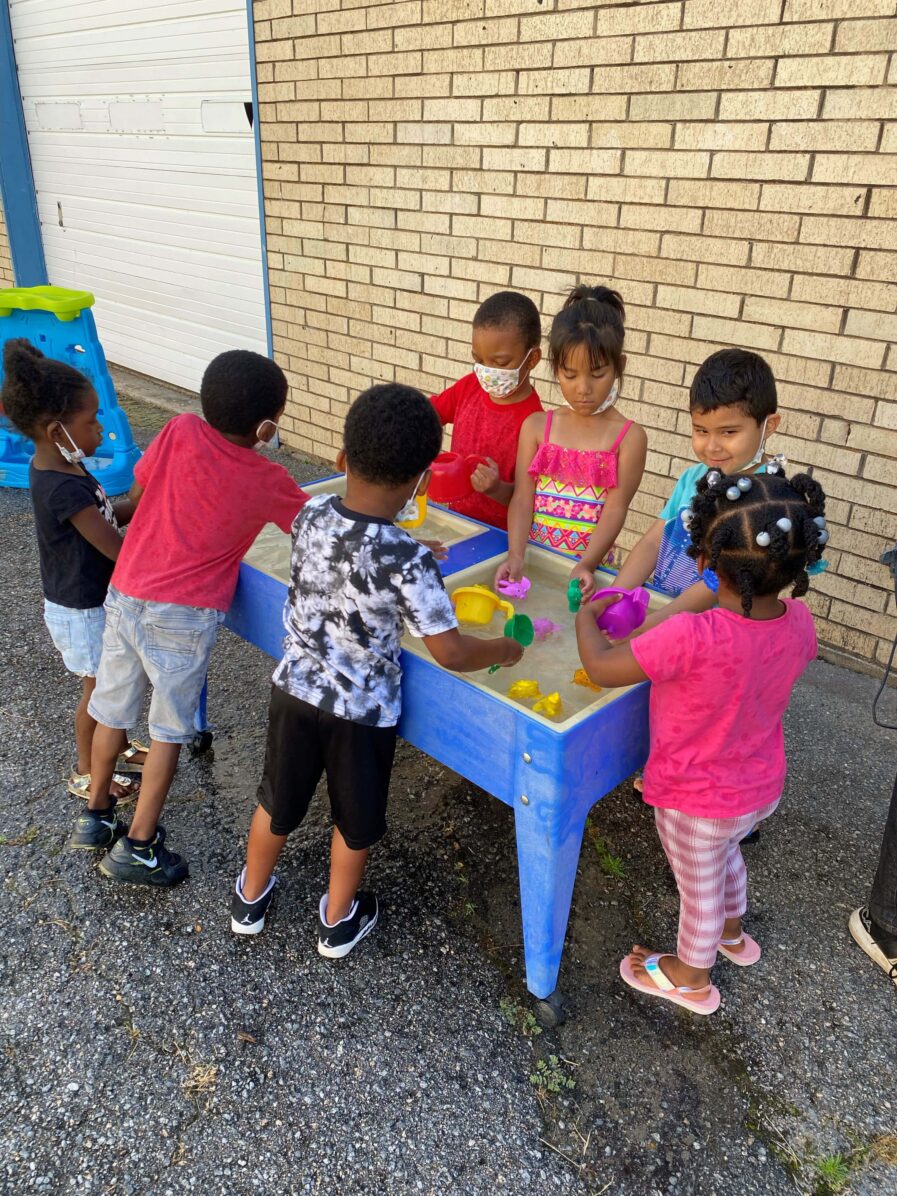 7 children stand around a water table playing with water