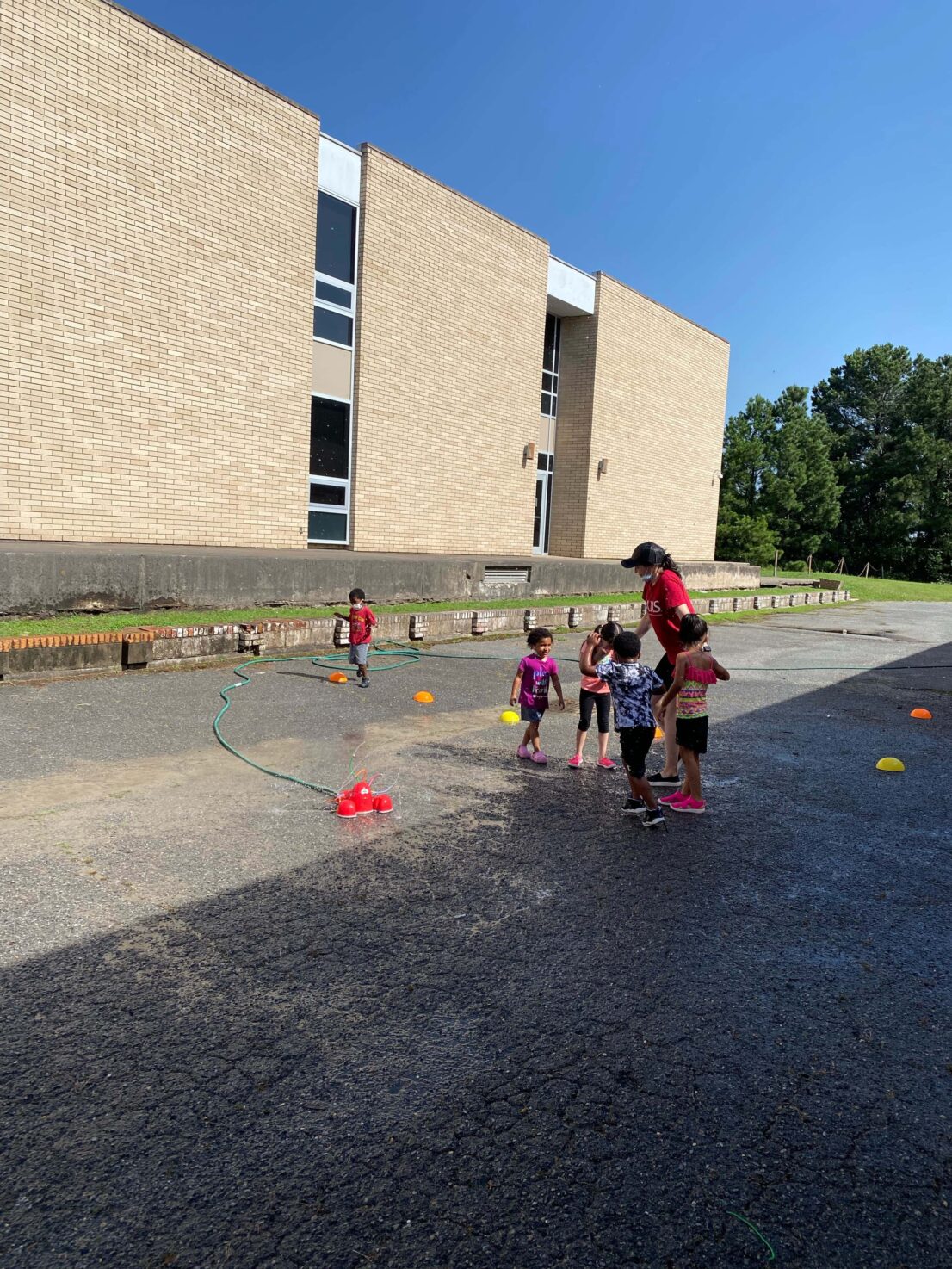 children playing in the sprinkler with their teacher