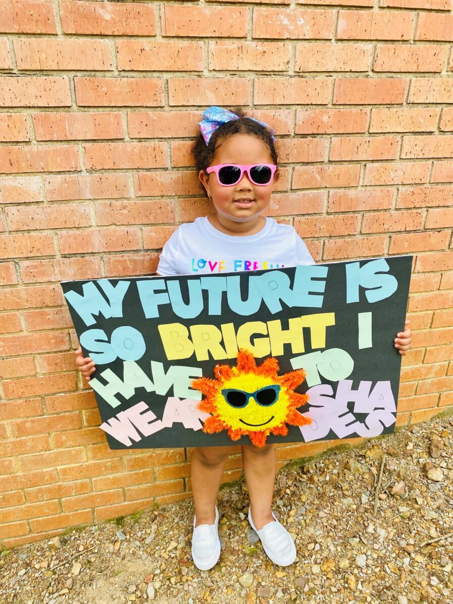 Girl wearing sunglasses holding a sign that says, 