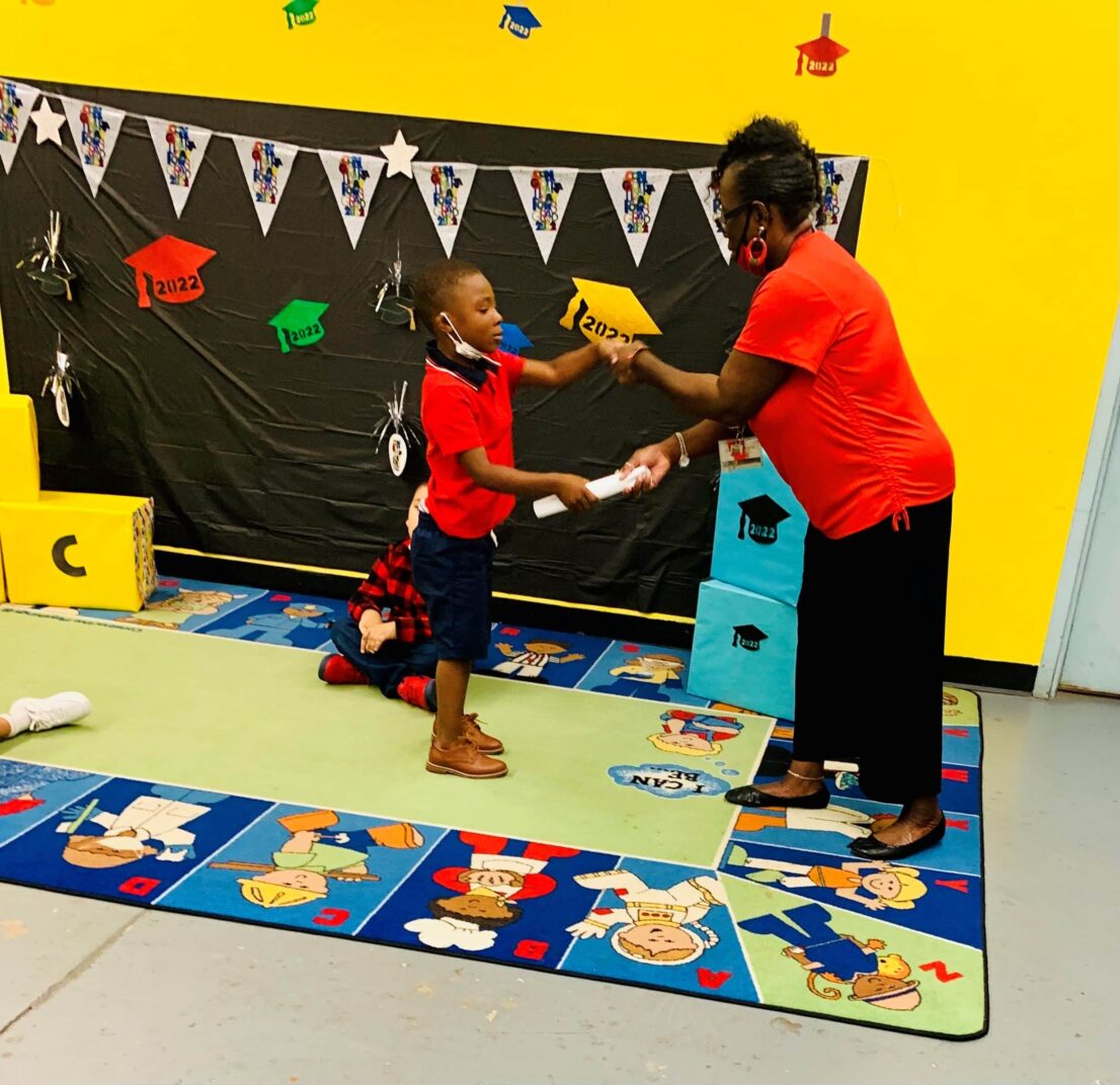 Teacher hands child his certificate for completing the Head Start program.
