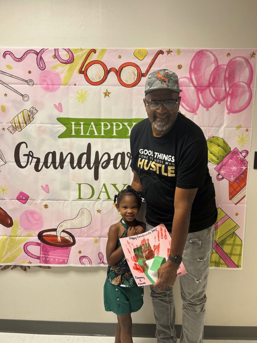 grandfather standing with granddaughter who is holding a picture they made