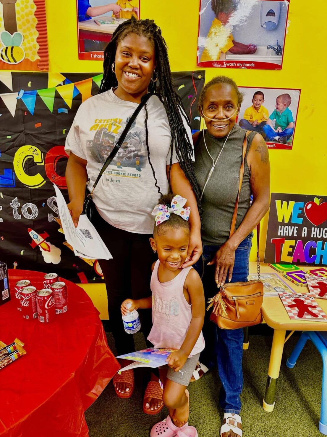 2 adults pose with a young girl in front of them who is holding a small bottle of water and a book