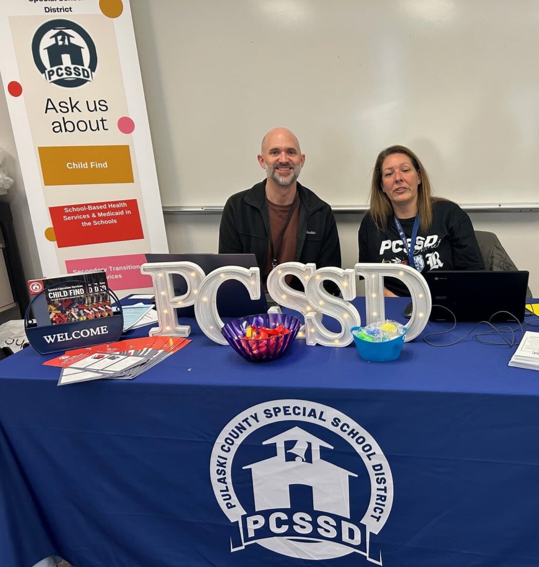 A man and woman from Pulaski County Special School District are sitting at a table waiting to help families with enrollment.