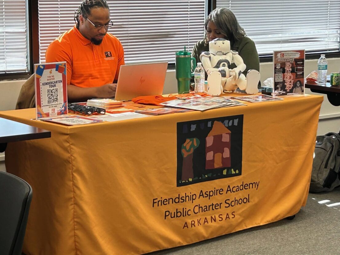 A man and woman from Friendship Aspire Academy are sitting at a table waiting to help families with enrollment.