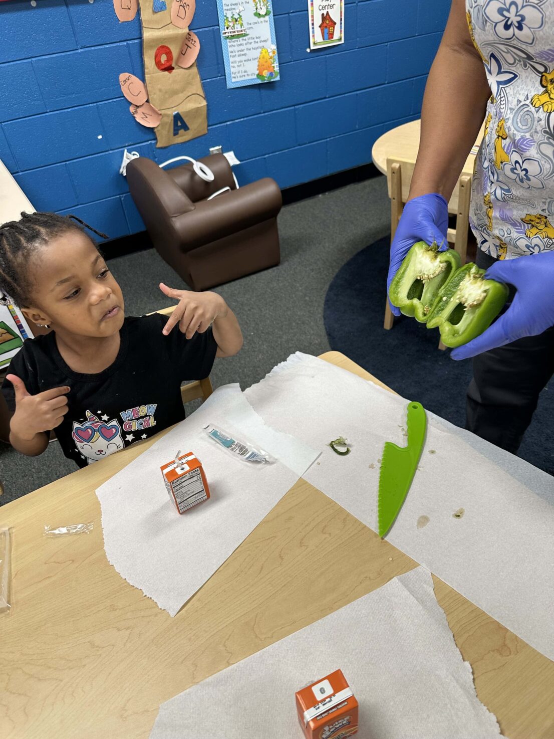 Teacher is showing a student how the green bell pepper looks on the inside after it was cut open. You can see the seeds of the bell pepper.