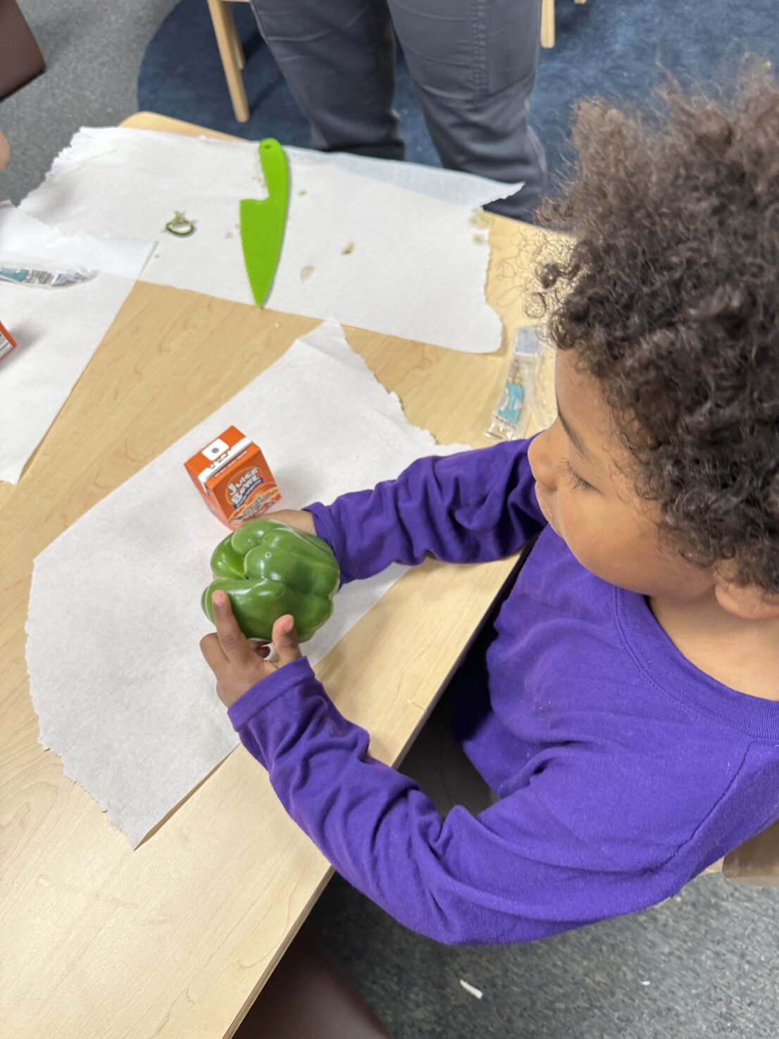 The student is holding the green bell pepper and looking at it.