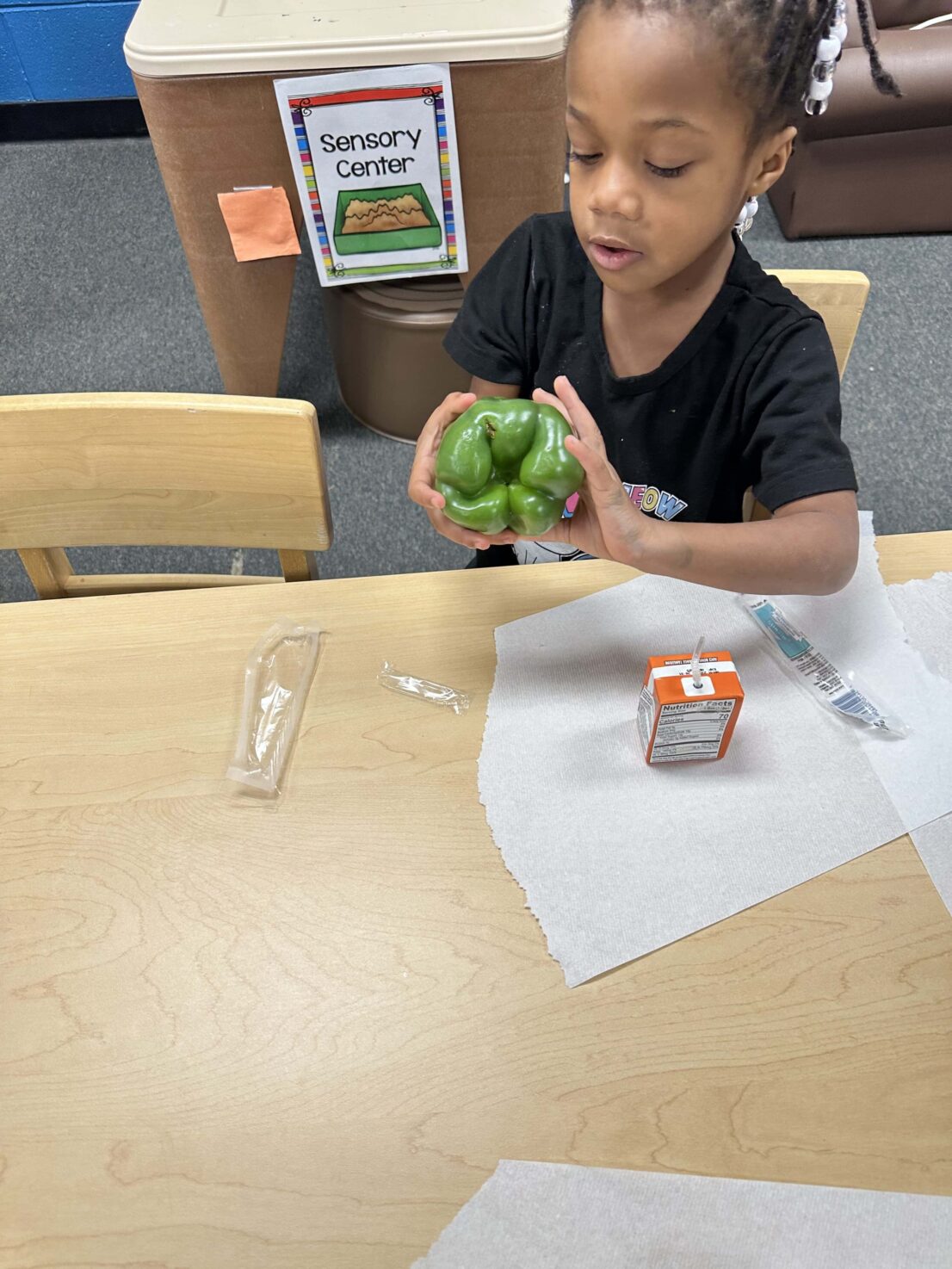 A student is holding and looking at the green bell pepper.