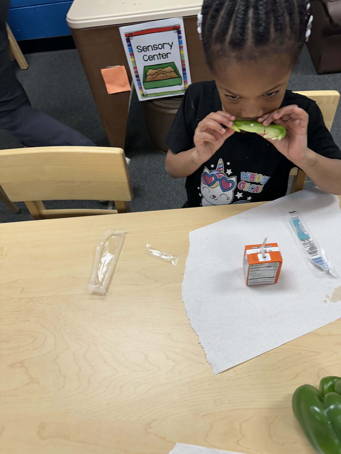 A student is holding and smelling a slice of the green bell pepper while sitting at the desk.